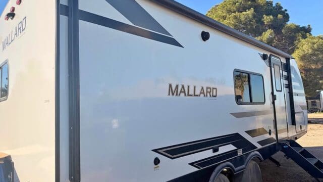White Mallard RV parked under clear sky.