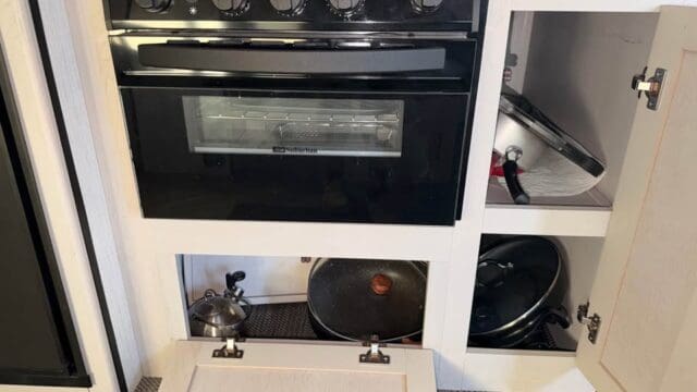 Black kitchen stove with open storage cabinets.