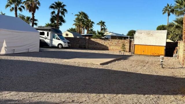Gravel lot with palm trees and building.