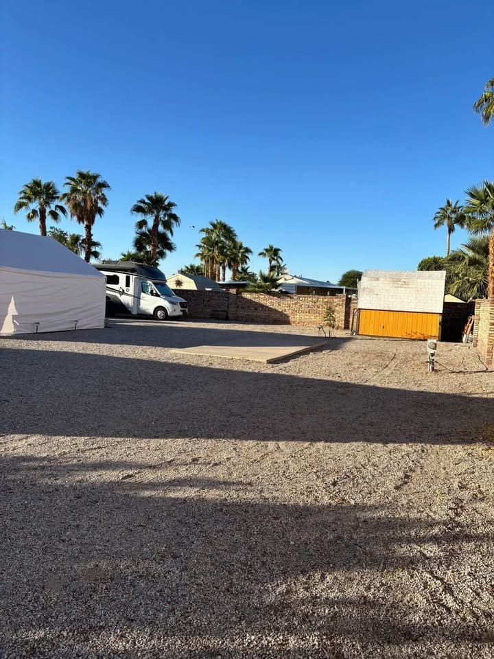 Gravel lot with palm trees and building.